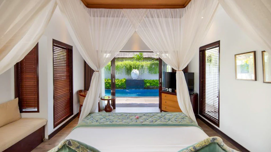 A luxurious bedroom with a white canopy bed opens to a private pool and tropical garden.