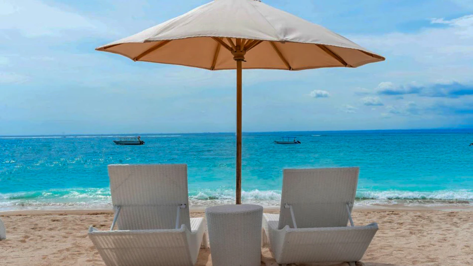 White lounge chairs and umbrella on a sandy beach overlooking the turquoise ocean at Nusa Lembongan.