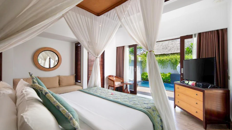 Luxurious resort bedroom with a four-poster bed and white netting, opening to a private pool.