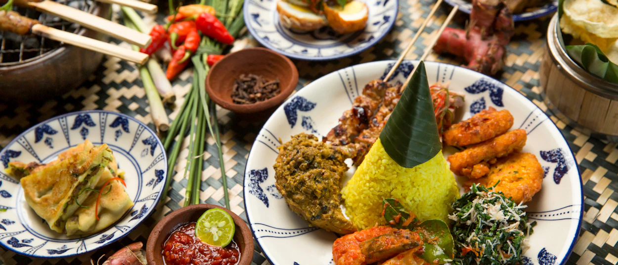 A beautifully arranged Balinese lunch with yellow cone rice, satay, and fresh vegetables in Ubud.