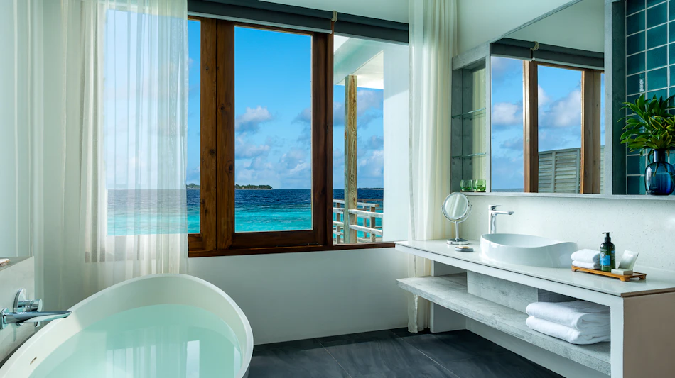 Luxurious bathroom in a Maldives water villa with a deep soaking tub and stunning ocean views.