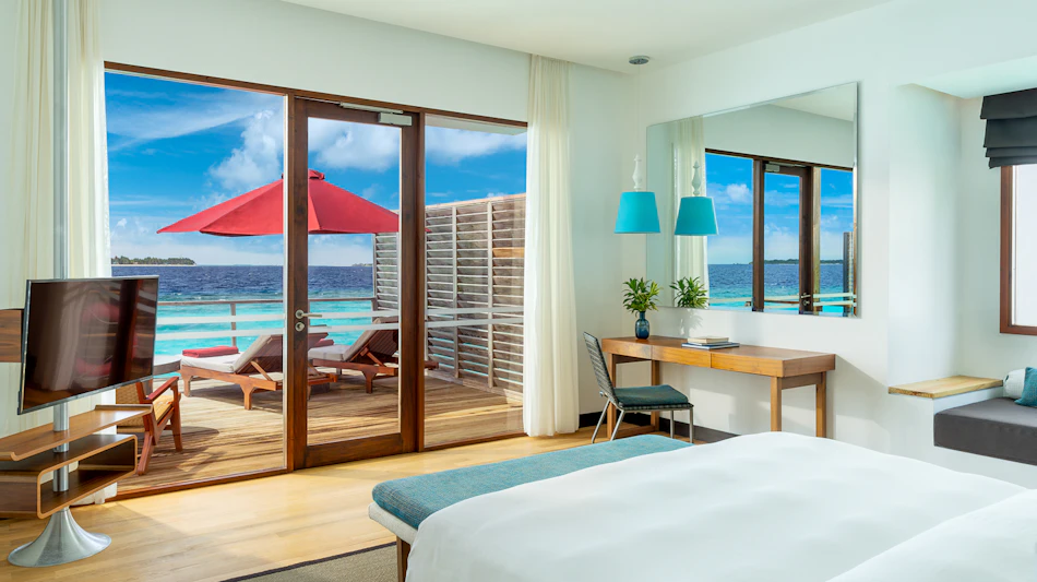 Luxurious water villa bedroom with a private deck, lounge chairs, and turquoise ocean views in the Maldives.