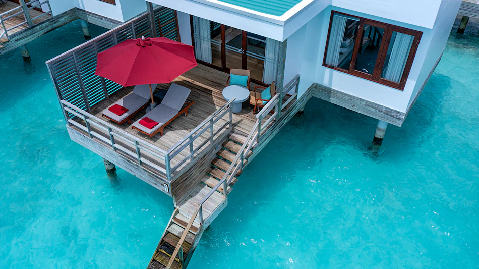 An overwater villa at Dhigali Maldives with a private deck, lounge chairs, and turquoise ocean.