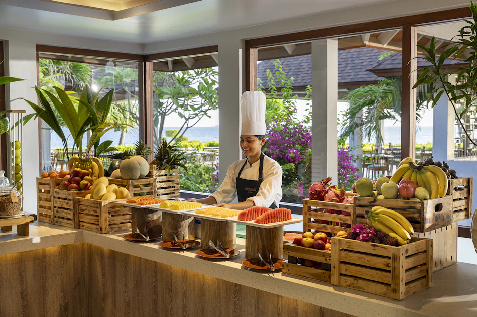 Smiling chef at an abundant fresh fruit buffet in a bright Maldives resort restaurant.