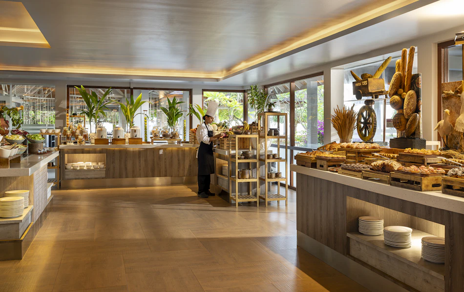 A chef arranges a lavish buffet spread with pastries and fruits in a bright, inviting resort restaurant.