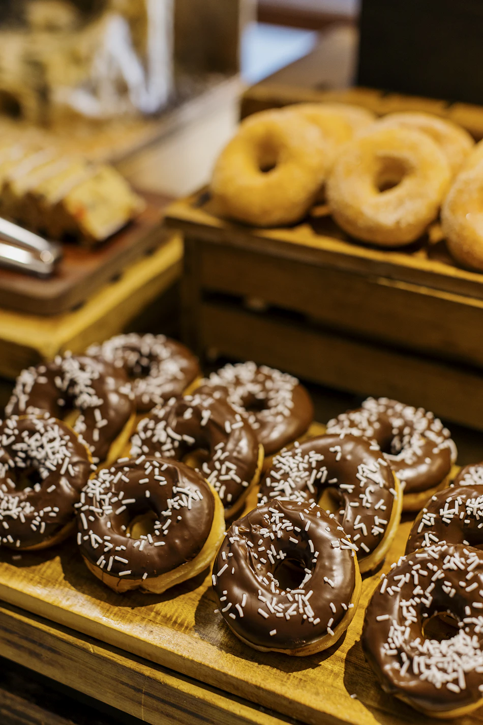 A tempting display of chocolate-frosted donuts with white sprinkles and plain donuts on a wooden buffet.