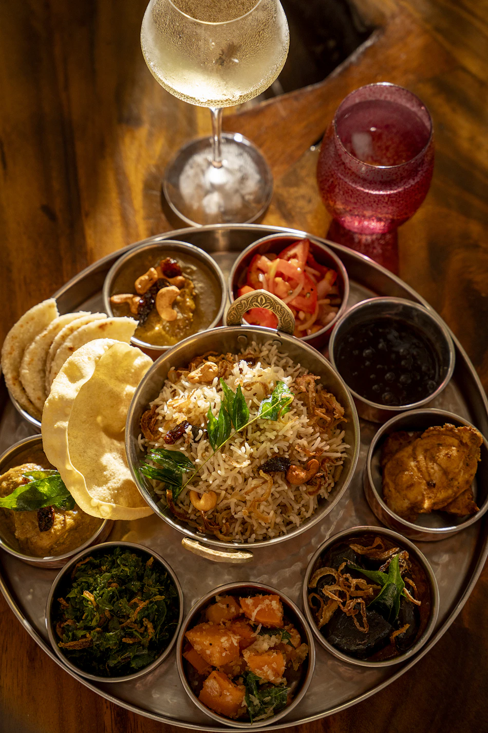 A gourmet thali meal featuring biryani, various curries, flatbreads, and wine, served at a Maldives resort.