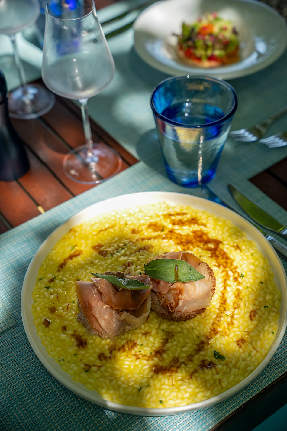 Delicious yellow risotto with prosciutto and basil on a sunny outdoor resort dining table.