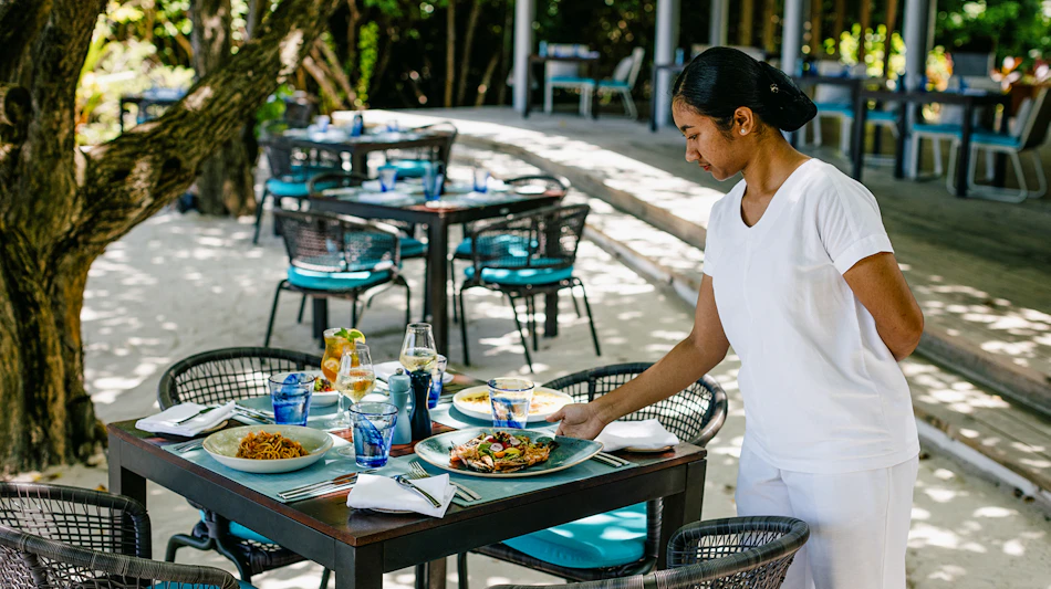 A server places a delicious meal on a table at a beautiful outdoor Maldives resort restaurant.