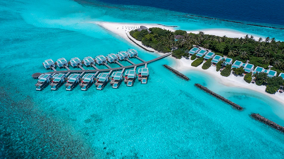 Luxurious overwater villas extend into turquoise water next to a white sand beach in the Maldives.