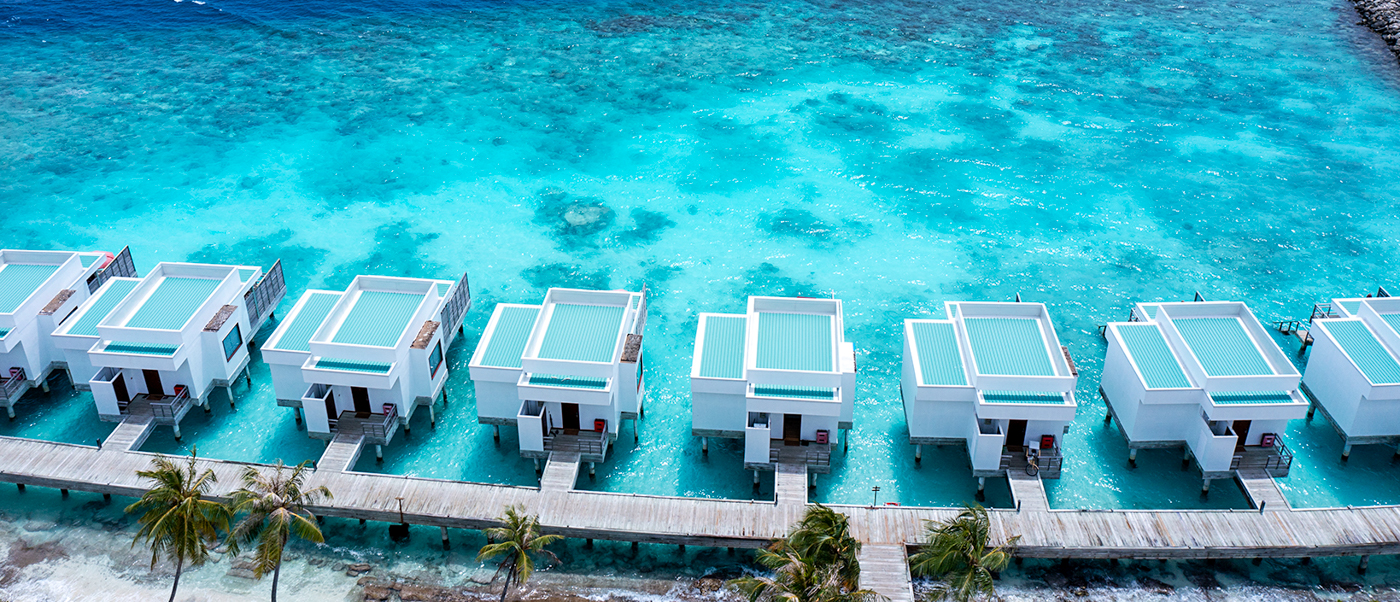 Aerial view of modern white overwater villas with private pools in the turquoise waters of Dhigali Maldives.
