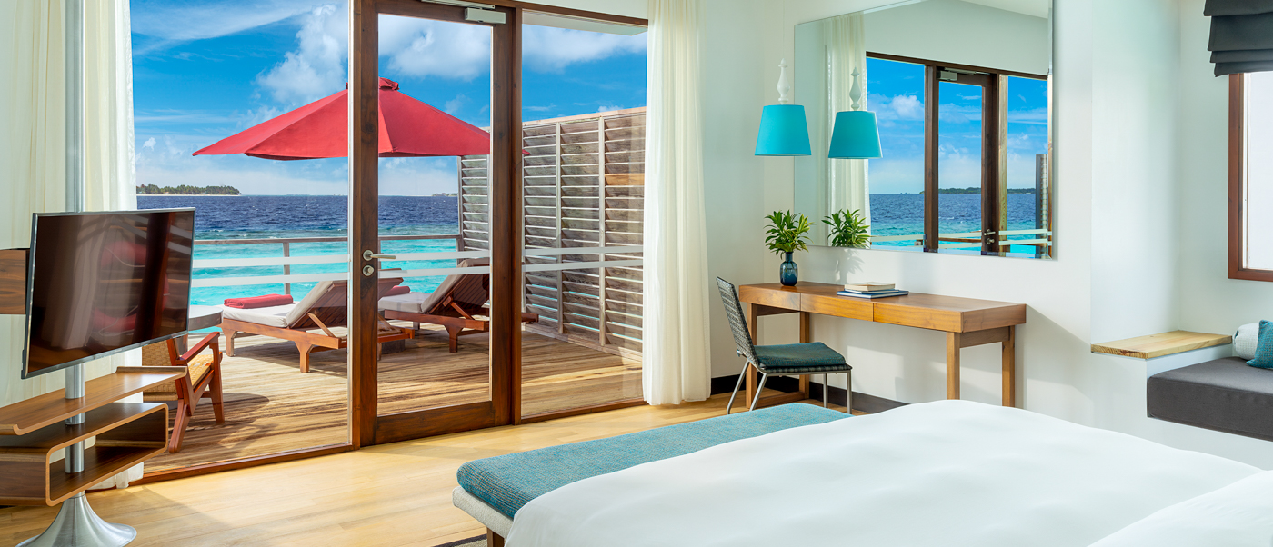 Luxurious water villa bedroom with a large bed, opening to an ocean deck in Dhigali Maldives.