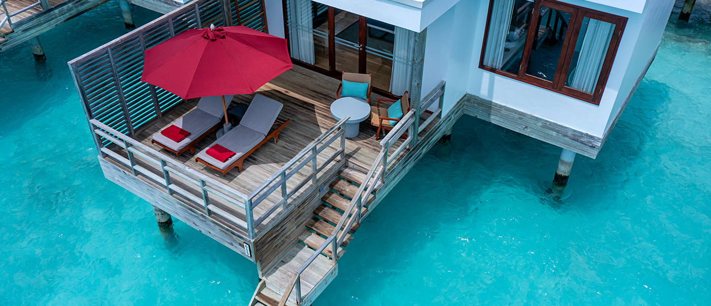 Luxurious overwater villa in Dhigali Maldives with a private deck, lounge chairs, and steps into turquoise water.