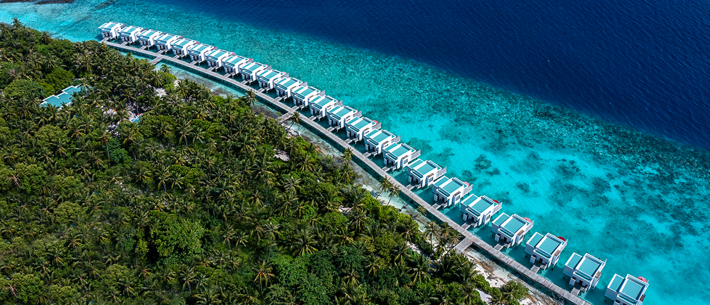 Aerial view of stunning water villas lining a lush green island in the Maldives with turquoise ocean.
