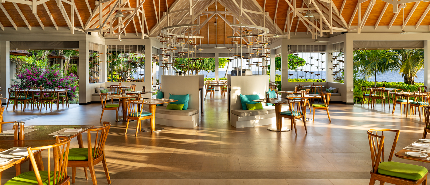 Spacious, open-air restaurant at Dhigali Maldives with high ceilings, wooden beams, and lush tropical views.