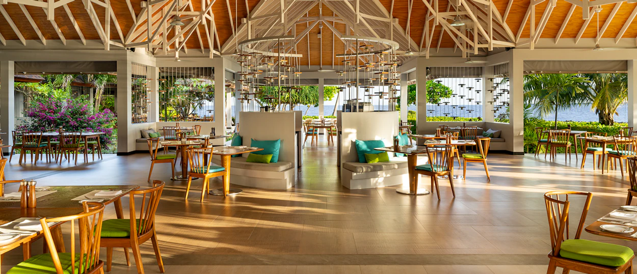 Spacious, open-air restaurant at Dhigali Maldives with high ceilings, wooden beams, and lush tropical views.