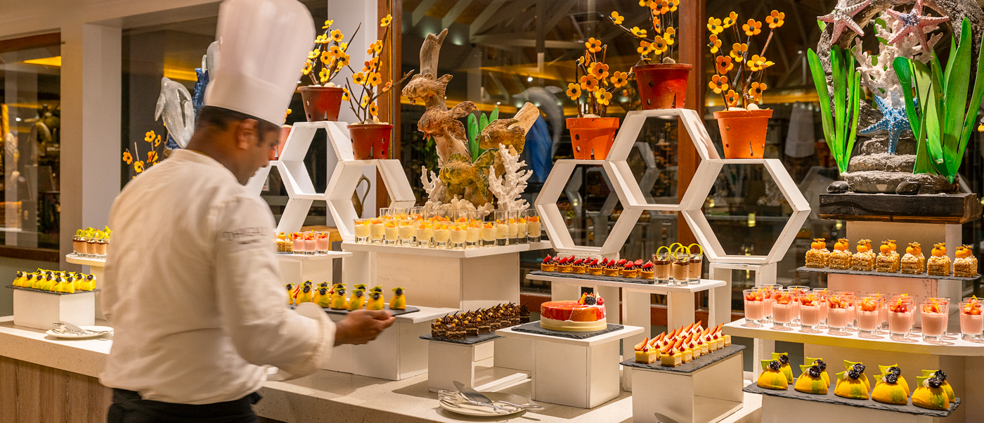 A chef arranges an array of colorful desserts on a beautifully decorated buffet at Dhigali Maldives.