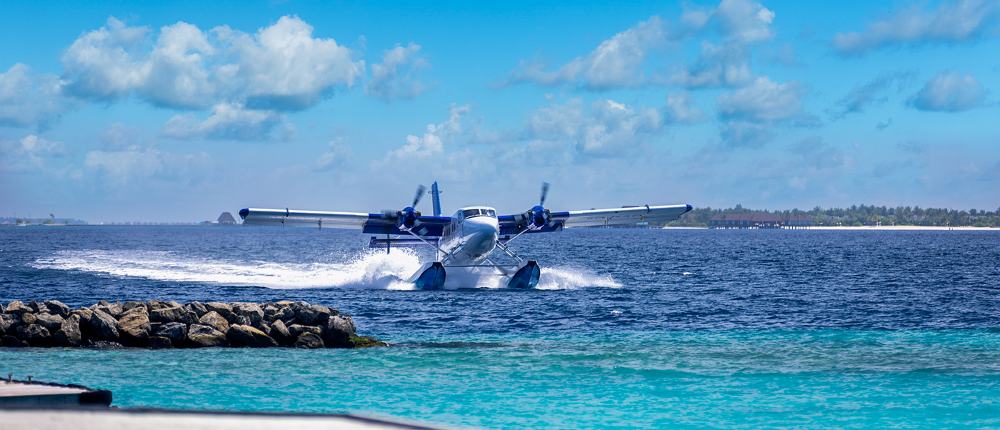 A seaplane lands on the clear turquoise waters of Dhigali Maldives under a blue sky.