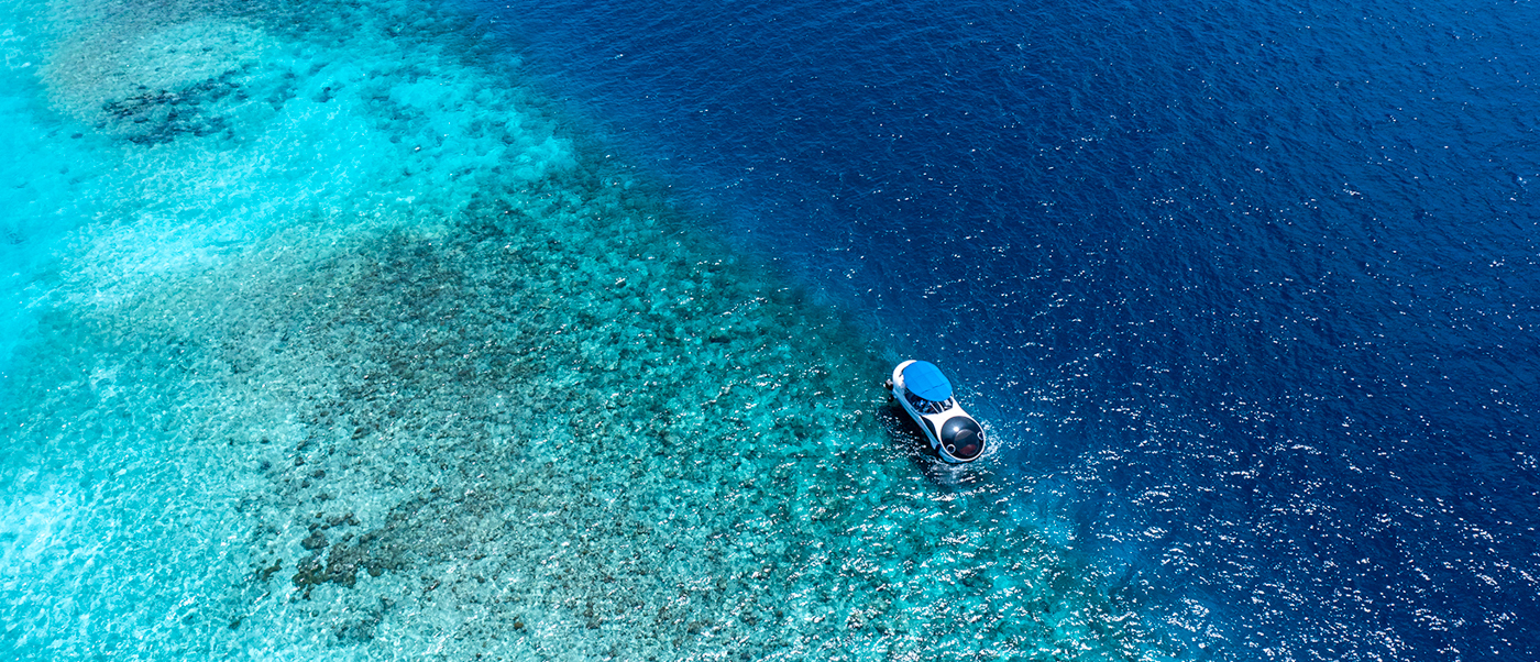 A white glass-bottom boat explores the shallow turquoise waters and coral reefs in the Maldives.