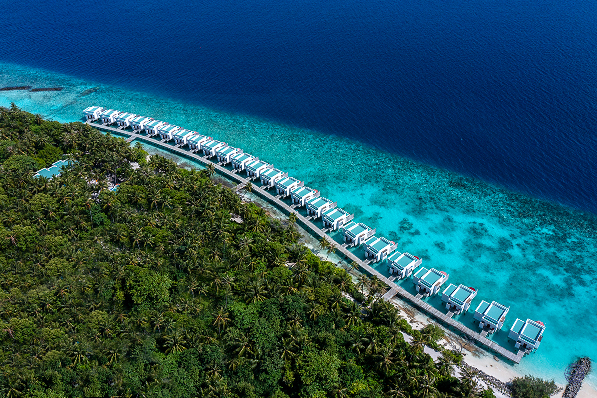 Luxurious water villas stretch over the clear turquoise waters of Dhigali Maldives, surrounded by lush island greenery.