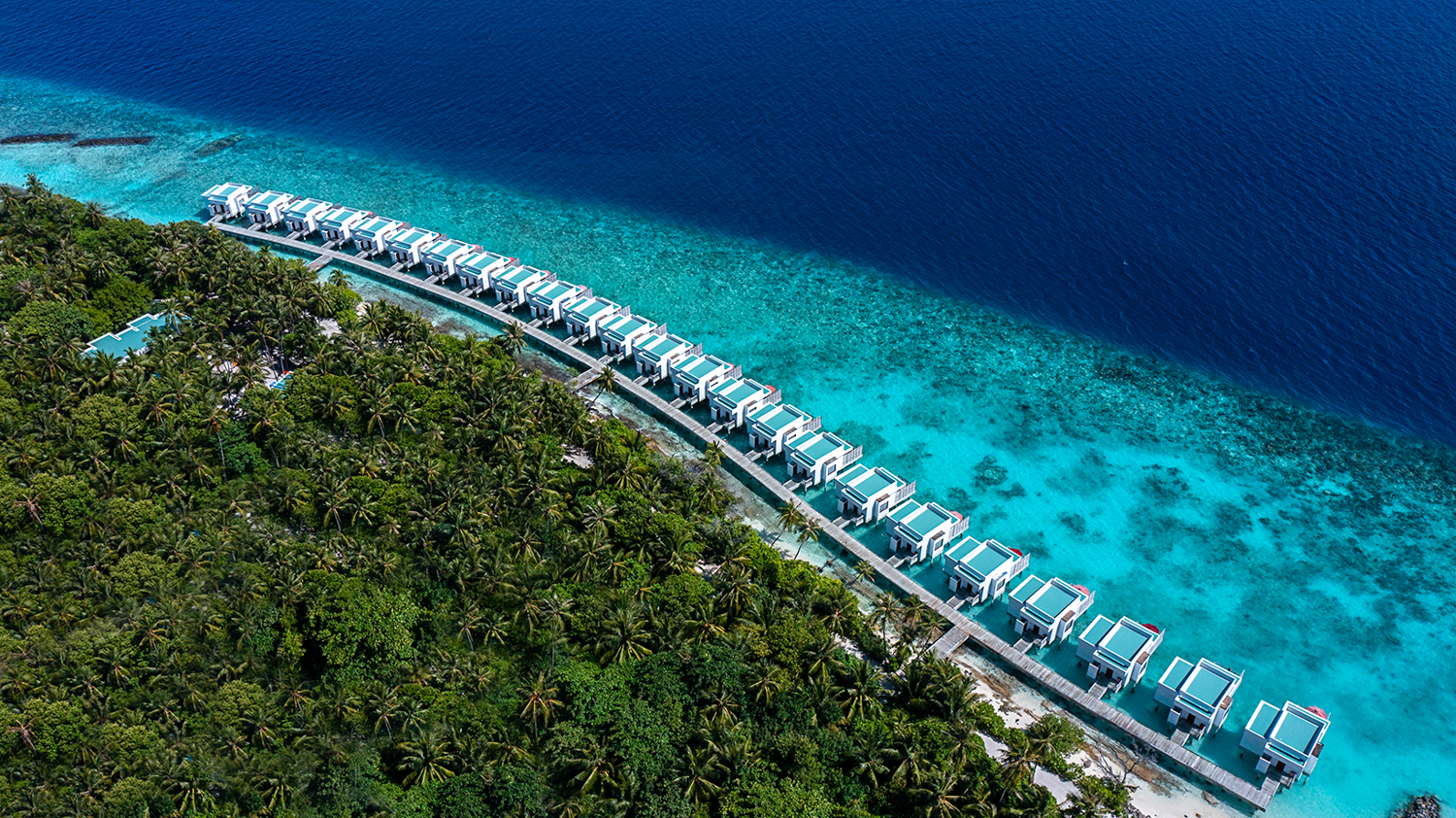Aerial view of luxury overwater bungalows extending into the clear turquoise ocean at Dhigali, Maldives.