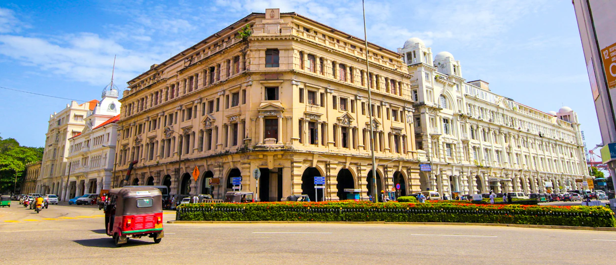 Ornate colonial-era buildings and a red tuk-tuk under a bright blue sky in Colombo.