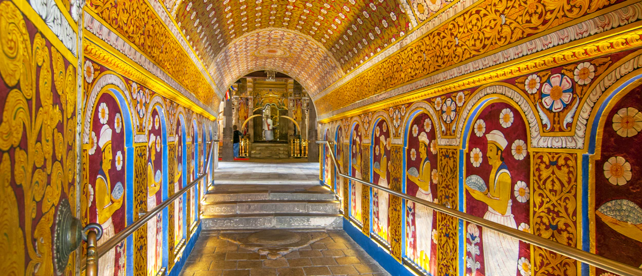 Ornate hallway inside Dambulla Cave Temple, showcasing golden ceilings and colorful ancient murals.