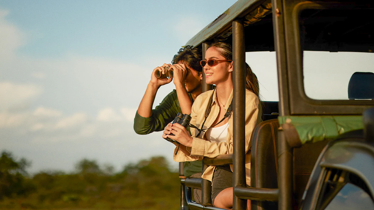 A happy couple enjoys a jeep safari in Yala National Park, spotting wildlife with binoculars.