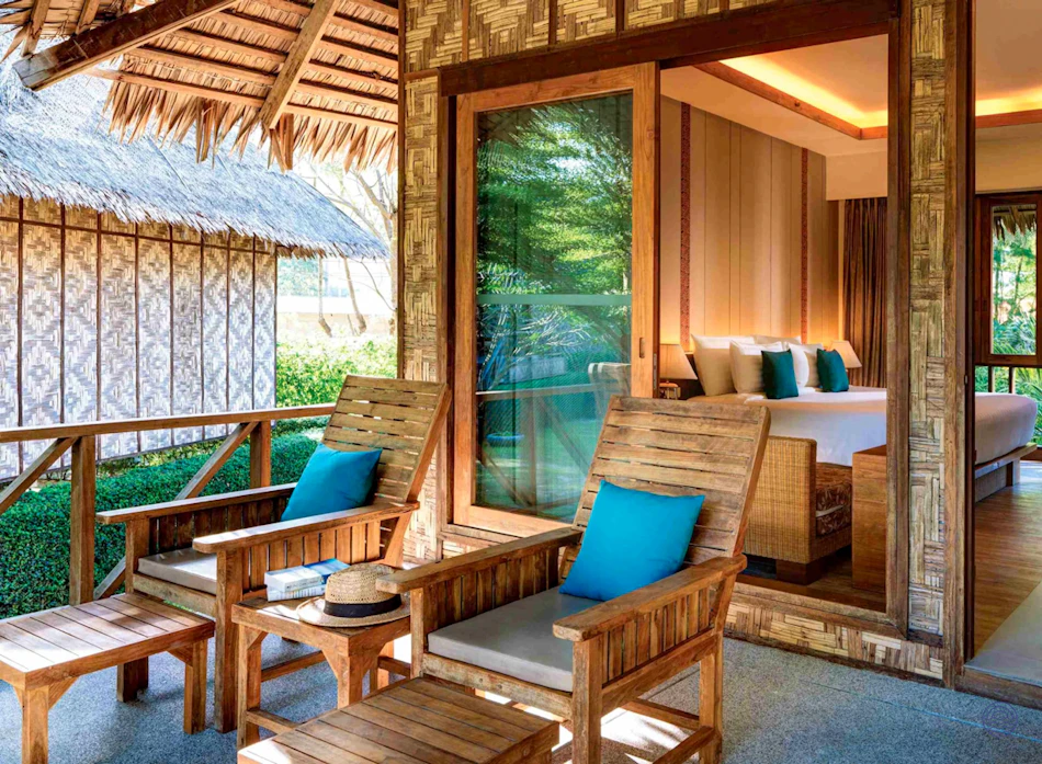 Tropical resort balcony with wooden lounge chairs and a view into a comfortable bedroom at SAii Village.