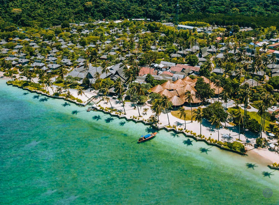 Koh Phi Phi resort with bungalows, palm trees, and a longtail boat on turquoise water.