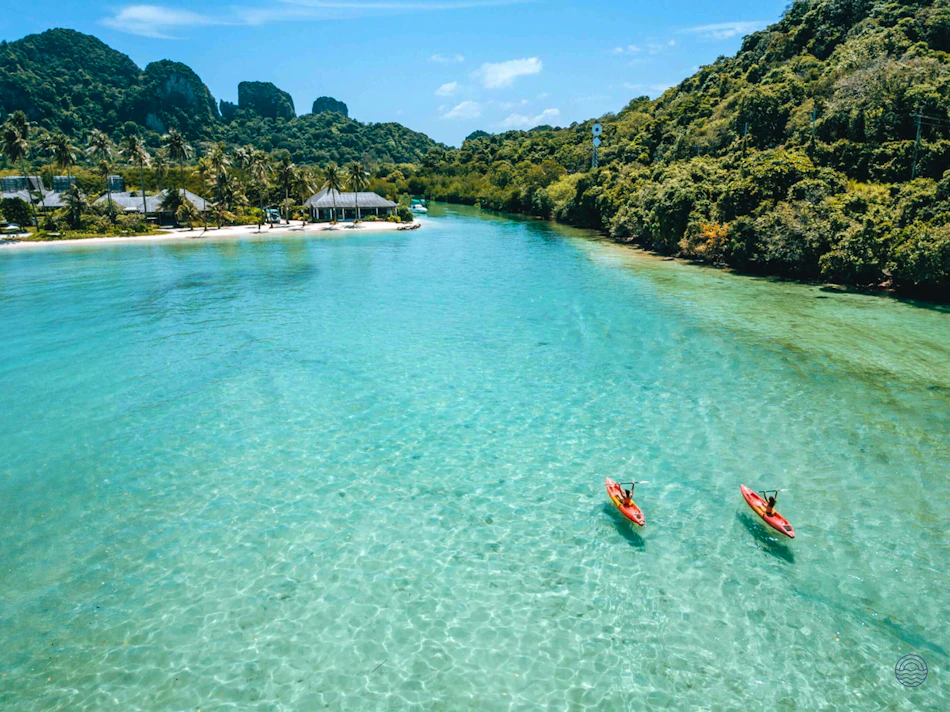 Two red kayaks paddle on clear turquoise water near the SAii Village Resort, Koh Phi Phi.