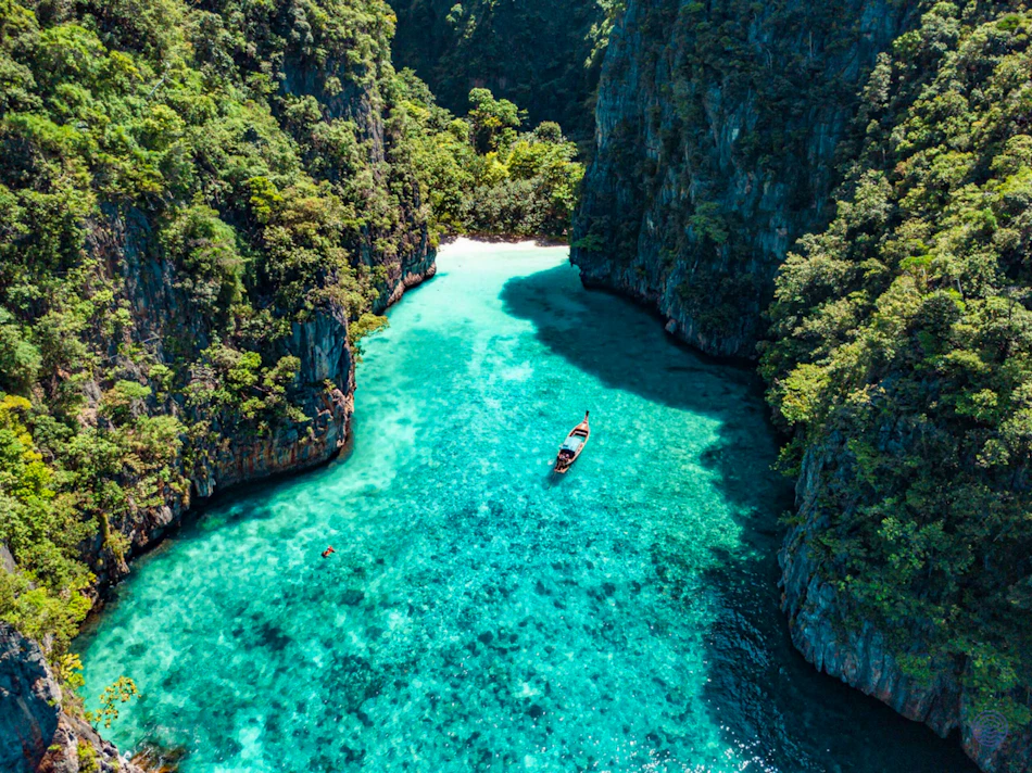 Longtail boat in a vibrant turquoise bay surrounded by towering green cliffs in Koh Phi Phi, Thailand.