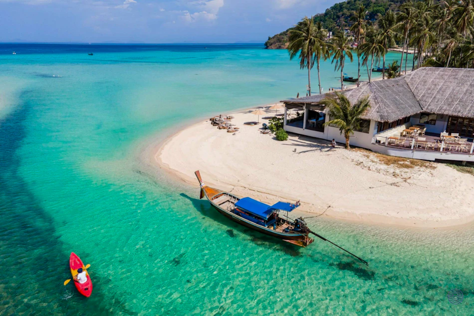 Idyllic tropical beach with a longtail boat, kayak, and resort building in Koh Phi Phi.