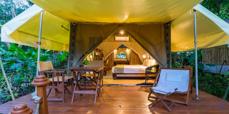 Comfortable glamping tent with a bed and outdoor seating on a wooden deck at Hintok River Camp.