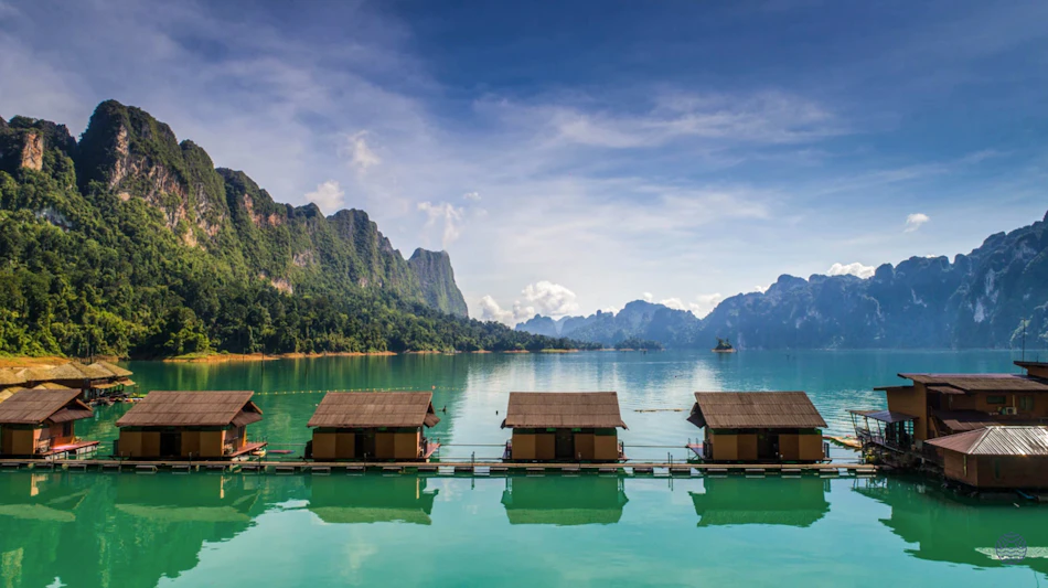 Floating bungalows on a tranquil turquoise lake surrounded by dramatic green limestone mountains in Khao Sok.