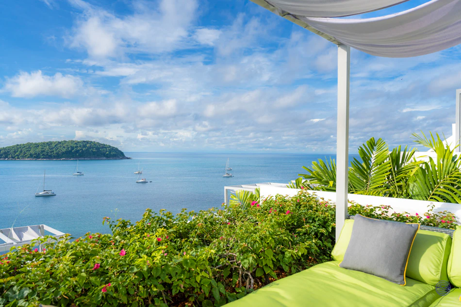 A serene green lounge overlooks the blue ocean with sailboats and a lush tropical island in Phuket.