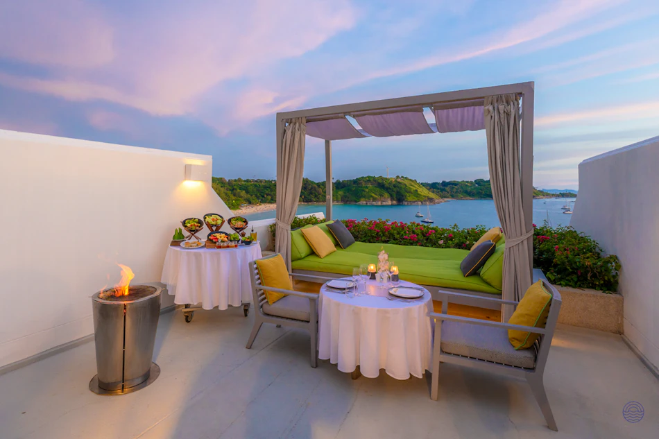 Romantic rooftop terrace at The Nai Harn, Phuket, with a daybed and sunset bay view.