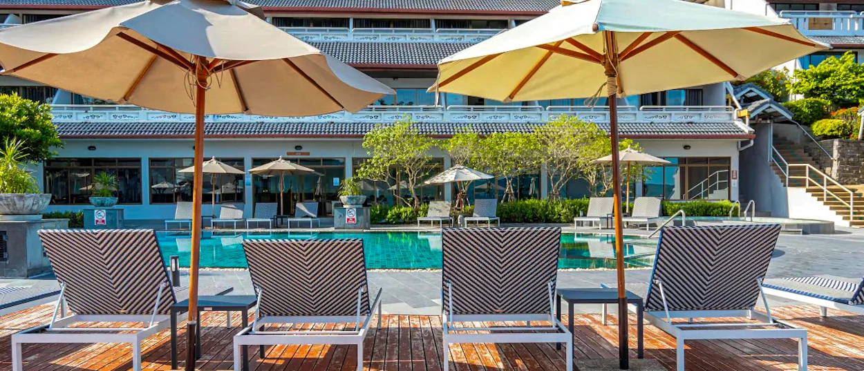 Two empty lounge chairs and umbrellas beside a tranquil resort swimming pool in Phuket, Thailand.