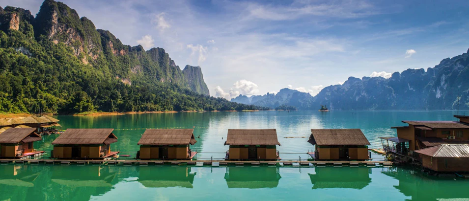 Traditional floating bungalows on a tranquil lake surrounded by majestic limestone mountains in Khao Sok, Thailand.