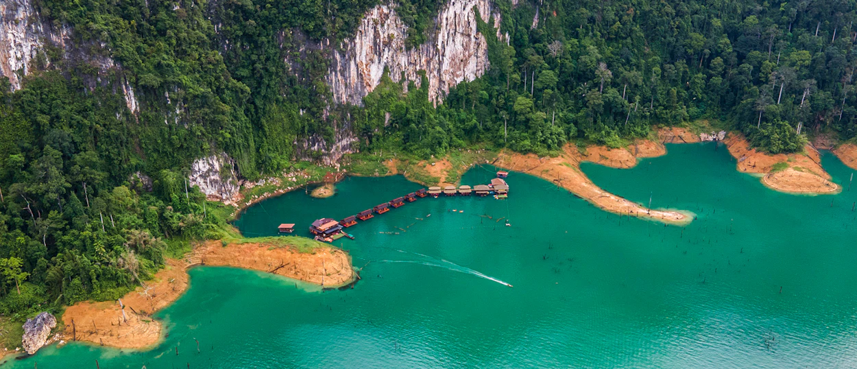 Floating bungalows on a serene turquoise lake in Khao Sok, Thailand, surrounded by lush jungle cliffs.