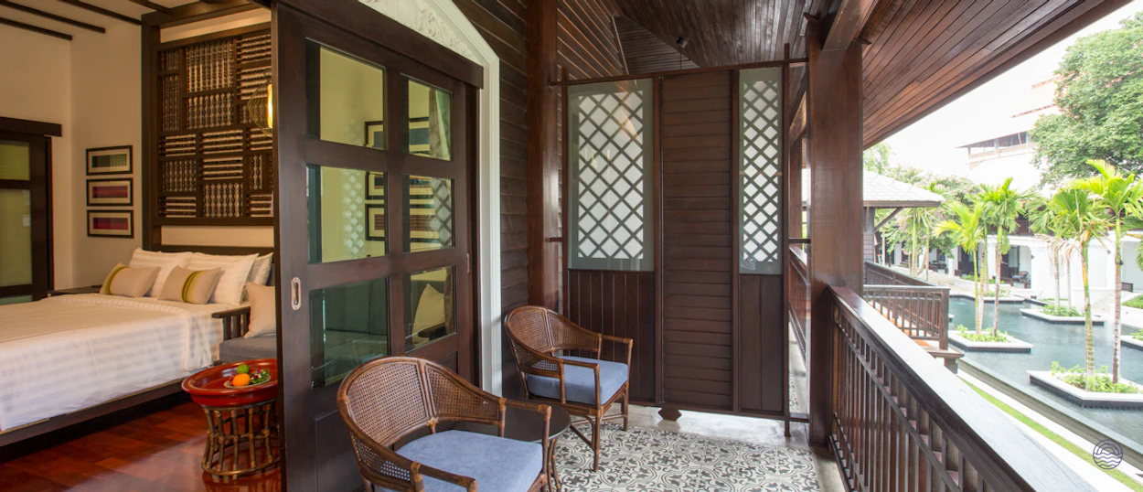 Luxurious traditional Thai resort room with a balcony overlooking serene water features and lush palm trees.