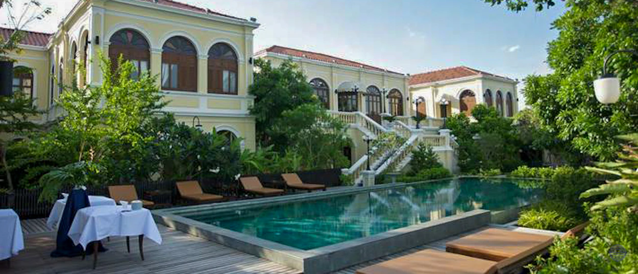 Elegant Bangkok hotel with a large swimming pool, sun loungers, and lush green gardens.