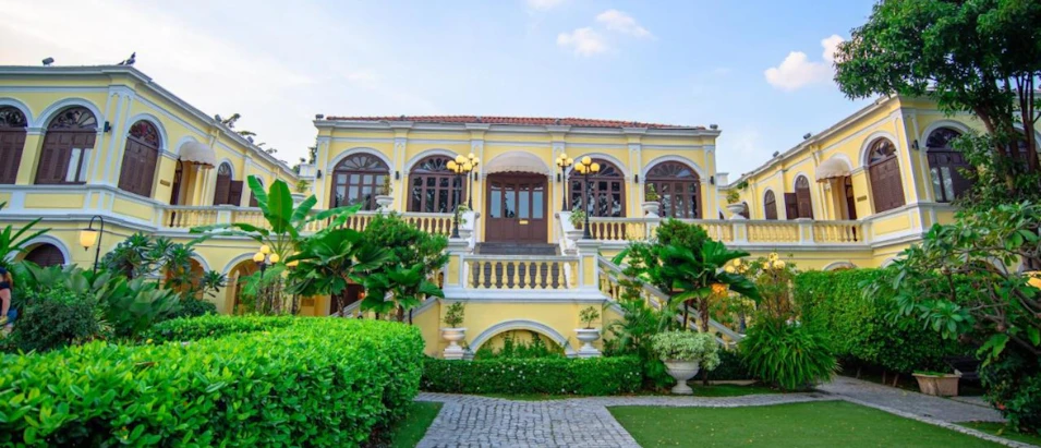 Elegant yellow Praya Palazzo hotel with a grand staircase and lush tropical gardens in Bangkok.
