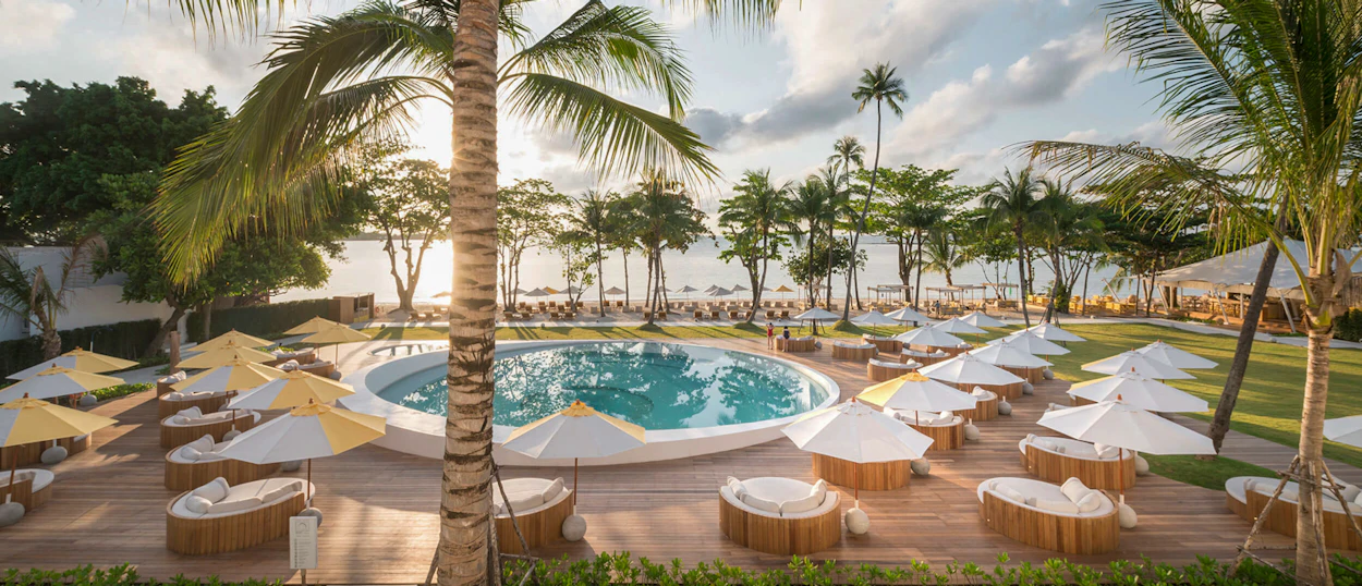 A luxurious resort pool with daybeds and palm trees overlooking the ocean in Koh Samui.