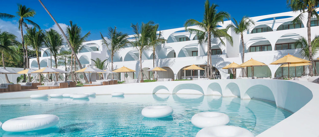 A modern white resort with palm trees and a large pool, featuring floating rings in Koh Samui.