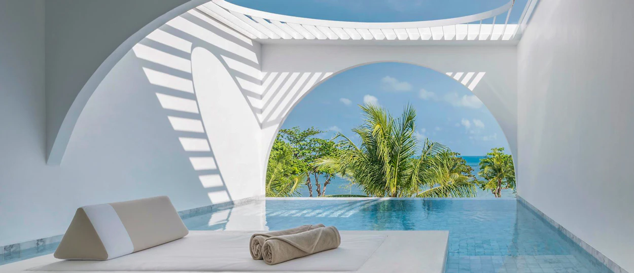 A luxurious white resort room with a private pool overlooking palm trees and the ocean in Koh Samui.