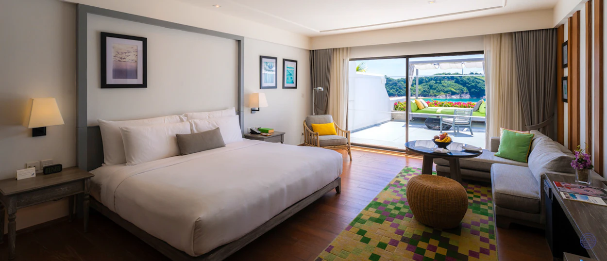 A luxurious hotel room in Phuket with a comfortable bed, sitting area, and a private balcony.