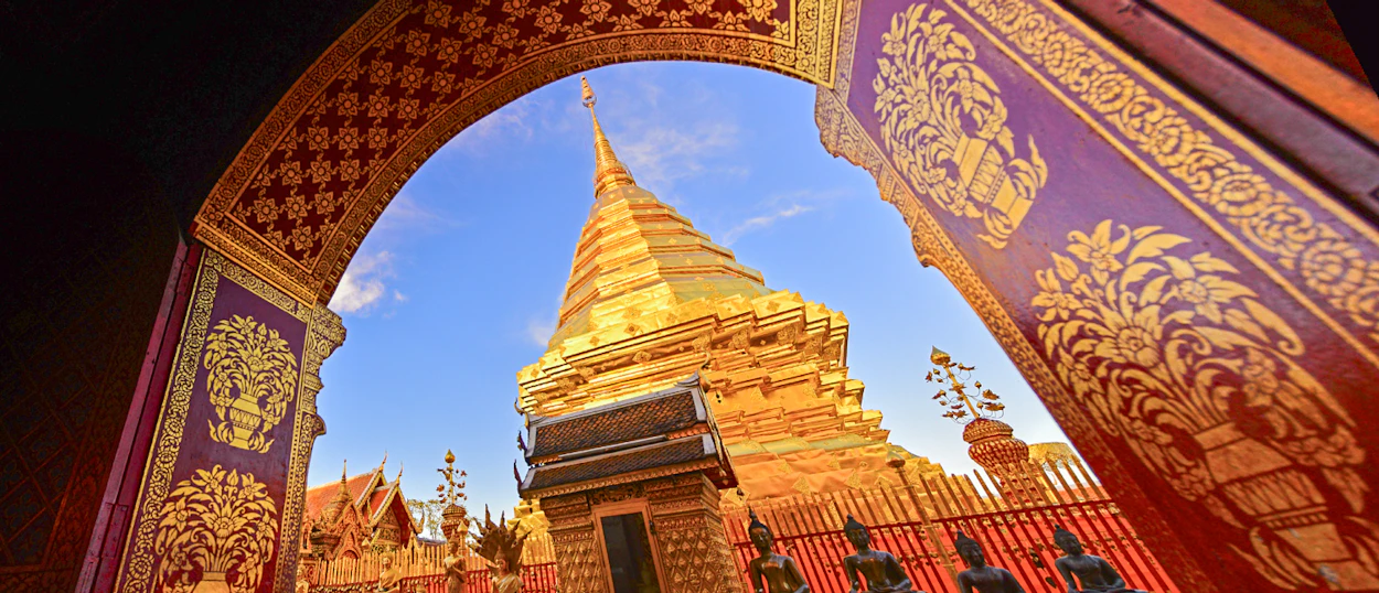 A majestic golden chedi at Doi Suthep Temple in Chiang Mai, framed by an ornate archway.
