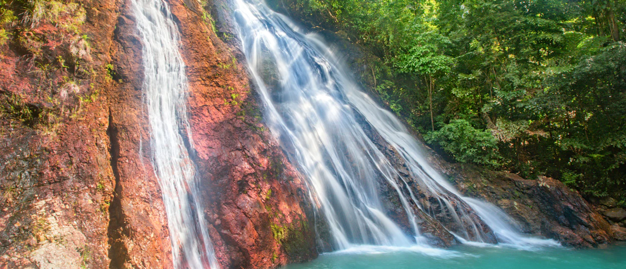 A stunning waterfall with clear blue water cascading over vibrant red rocks in Koh Samui.