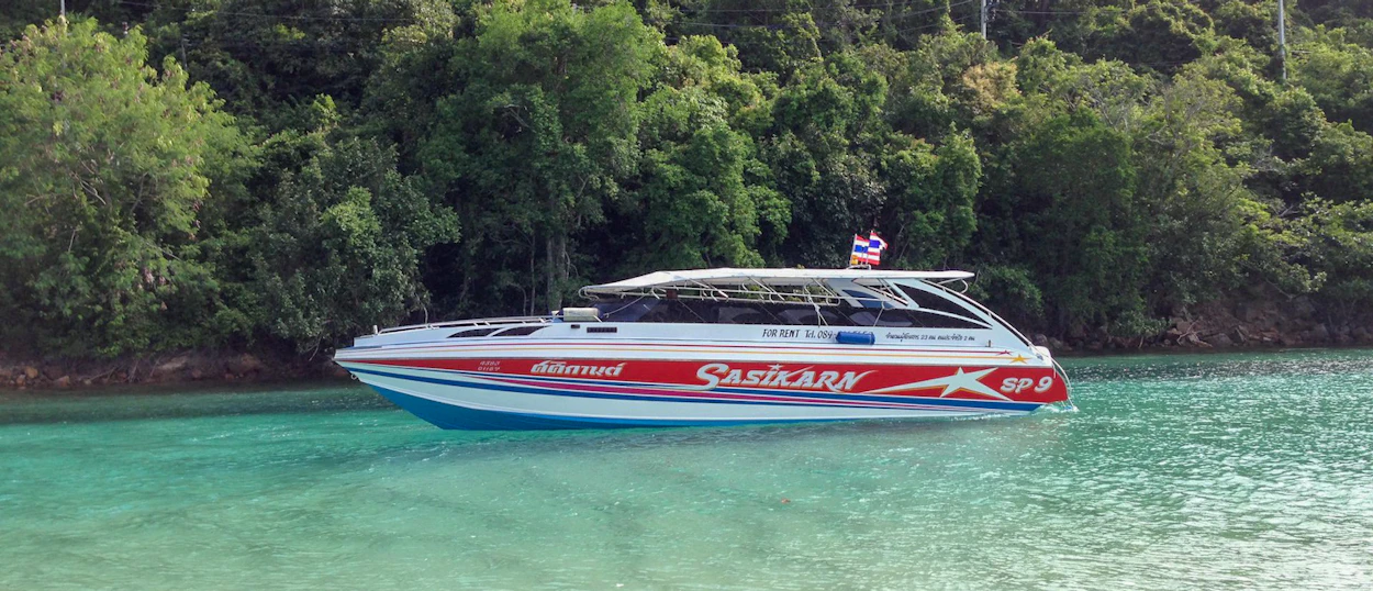 A white and red speedboat with a Thai flag cruises on the clear turquoise waters of Koh Phi Phi.
